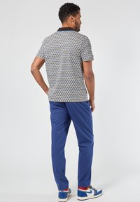 Lyhythihainen kuvioitu polo-paita ruskealla kauluksella, yhdistettynä sinisiin housuihin ja värikkäisiin sukkiin, joilla on siniset lenkkarit.