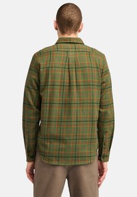 Groen geruit shirt van flanel, met oranje en zwarte lijnen, knopenmanchetten en een rugplooi voor beweging.