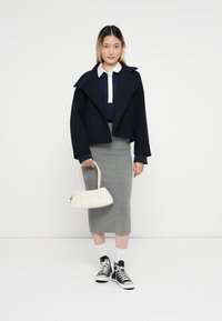 Abrigo corto navy, camisa blanca con cuello, falda lápiz gris, zapatillas negras y un bolso crema. Tela texturizada, diseño moderno, acentos simples.