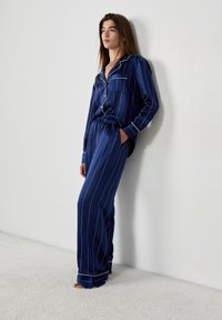 Navy blue pasiaste piżamy wykonane z gładkiego materiału, z koszulą zapinaną na guziki i kieszenią oraz spodniami z elastyczną talią w kontrastowe białe paski.