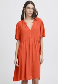 Rochie portocalie dintr-un material ușor. Dispune de mâneci scurte, decolteu în V și o siluetă fluidă care ajunge până la jumătatea gambei.
