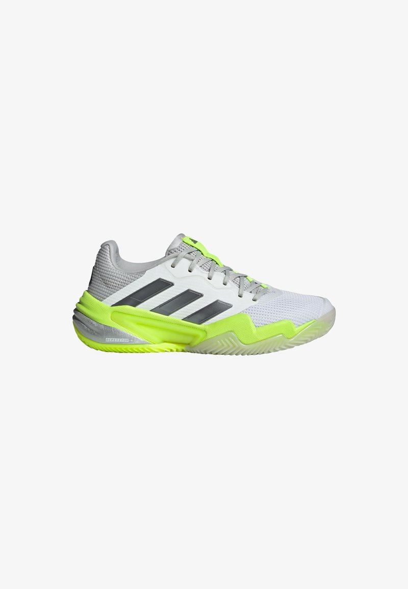 Sapitão atlético cinza e branco com detalhes em verde e superior em malha texturizada. Apresenta três riscas pretas e uma sola em padrão zigzag.