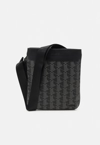 Mustast sünteetilisest materjalist kott, millel on geomeetriline muster. Kotil on lame põhi ja reguleeritav õlarihm.