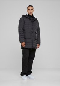 Svart quiltet boblejakke med hette, med frontknapper, to store frontlommer og et strømlinjeformet design. Stylet med svarte bukser og hvite sko.