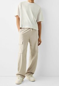 Jasnoszara koszulka z krótkim rękawem o luźnym kroju, zestawiona z beżowymi spodniami cargo z bocznymi kieszeniami i elastycznym pasem.