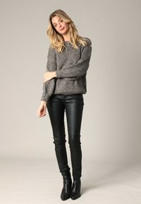 Pull en tricot gris avec une coupe décontractée et une texture côtelée, associé à un pantalon skinny en cuir noir et des bottines noires.