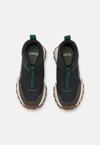 Black athletic shoes with a zip closure, green accents, and a textured outer. Features a brown, rugged sole and a cushioned interior.