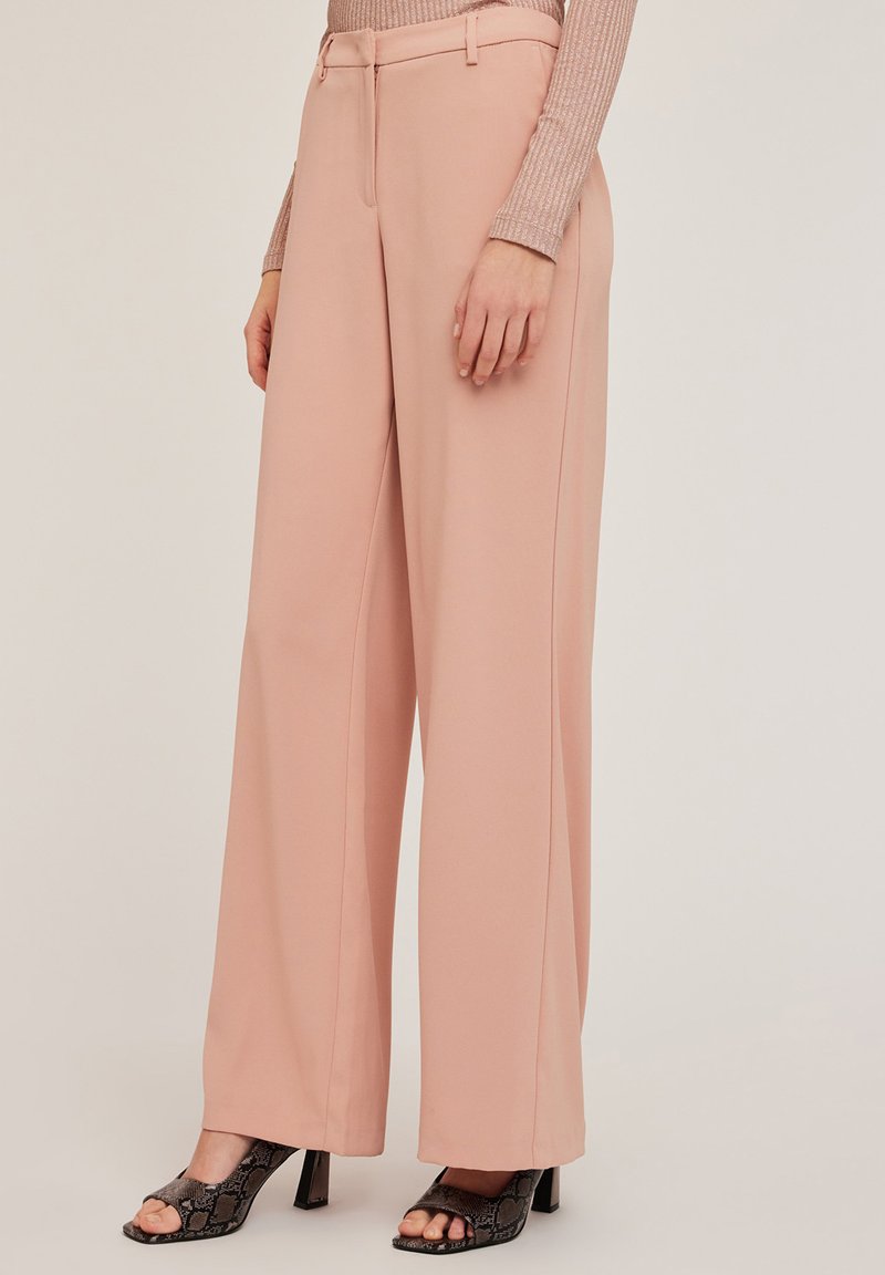 Pantalons larges rose clair en tissu lisse, dotés d'une fermeture éclair à l'avant, de passants de ceinture et de deux poches latérales.