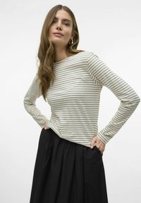 Langemouwen top in crèmekleur met smalle zwarte strepen, met een ronde halslijn en een ontspannen pasvorm, gecombineerd met een zwarte rok.