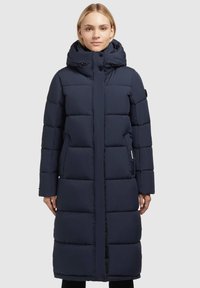 Navyblauwe gewatteerde lange jas met een hoge kraag, rits- en knoopsluiting, en zijzakken. Glad stof met gestikte quiltsecties.