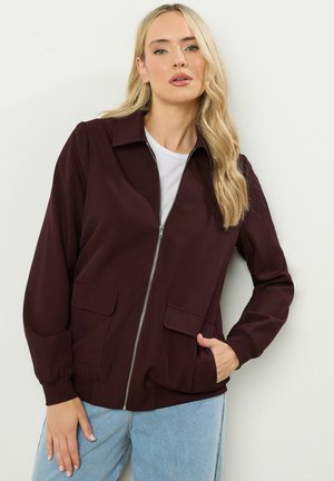 Bordeaux jasje met een ritssluiting aan de voorkant, kraagontwerp en twee voorzakken; gemaakt van zachte stof met een relaxte pasvorm en ribgebreide manchetten.