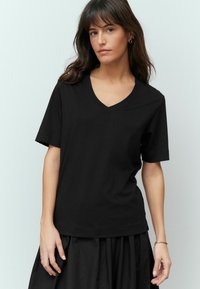 Zwarte katoenen V-hals t-shirt met korte mouwen en een relaxte fit. Gladde textuur, minimalistisch ontwerp, gecombineerd met een zwarte rok.