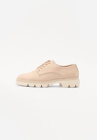 Scarpa beige in suede con lacci, punta rotonda e suola spessa di colore chiaro. Presenta cuciture semplici e dettagli di design minimalisti.