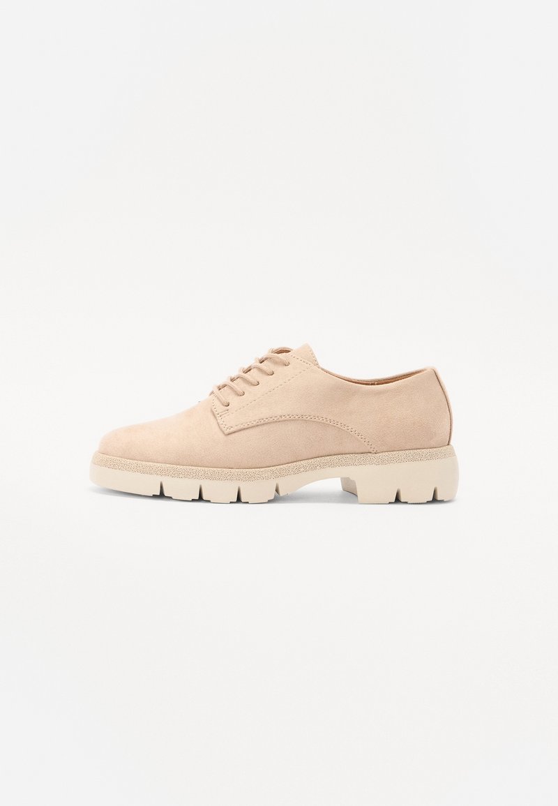 Scarpa beige in suede con lacci, punta rotonda e suola spessa di colore chiaro. Presenta cuciture semplici e dettagli di design minimalisti.