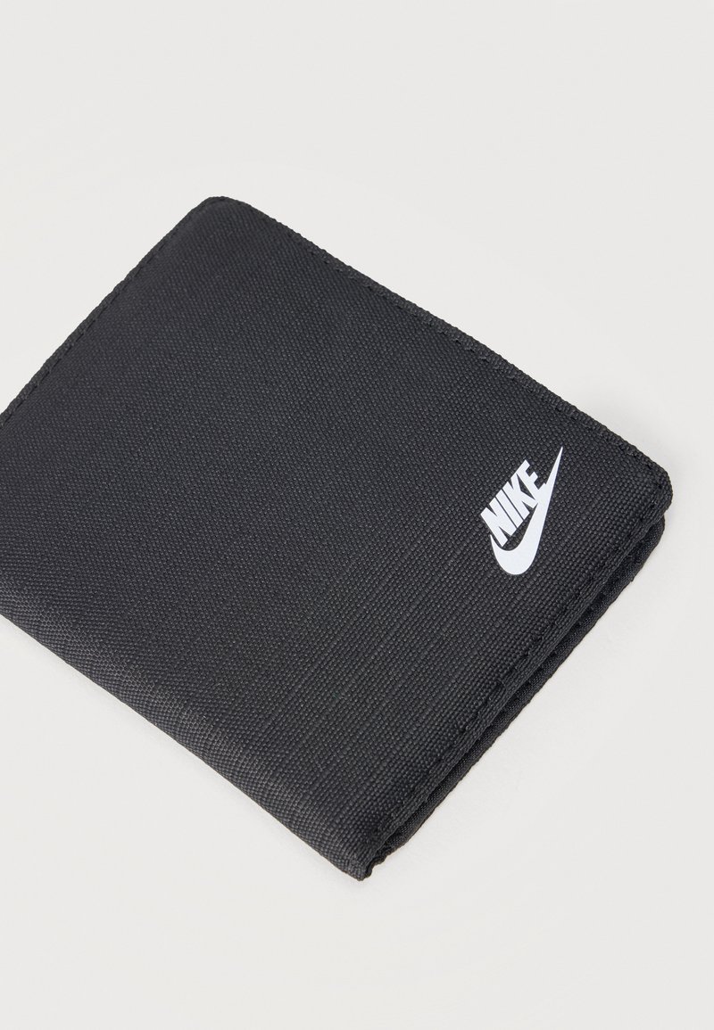 Portefeuille pliable en tissu noir avec logo blanc Nike dans un coin, présenté fermé sur un fond clair.