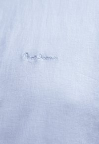 Ανοιχτό μπλε ύφασμα με διακριτικό κεντημένο λογότυπο "Pepe Jeans" σε νήμα που ταιριάζει κοντά στο κέντρο.