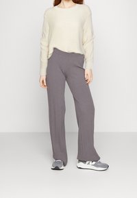 Grijze ribgebreide broek met een wijde pijp en een tailleband op halverwege de heupen, gecombineerd met een crème trui en grijze sportschoenen.