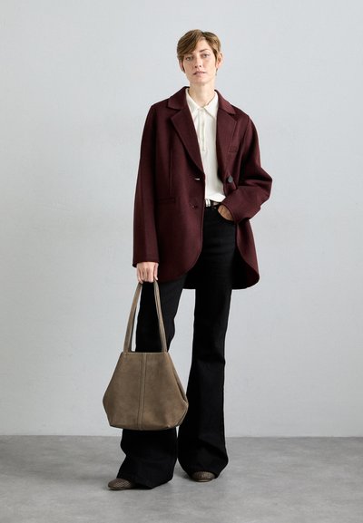 Blazer oversize borgogna, camicia bianca con bottoni, pantaloni neri a gamba larga, borsa a mano in suede grigio, scarpe con texture. Sfondo neutro.