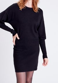 Abito in maglia nera con vestibilità morbida, dotato di maniche lunghe, texture a coste nella parte inferiore e una parte superiore liscia. Design minimalista.