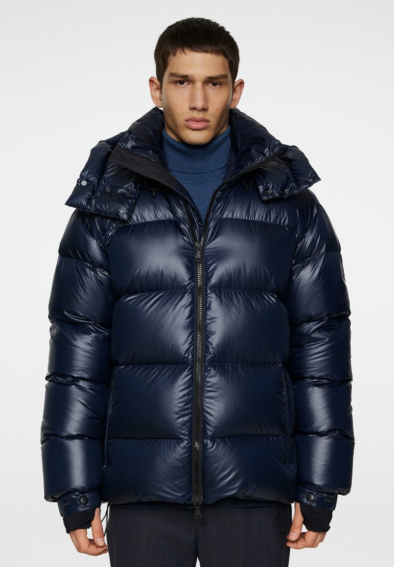 Navy puffer jacket with a glossy finish, featuring a zip closure, adjustable cuffs, and a high collar with a detachable hood.
