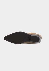 Ανδρική μπεζ σουέντ μπότες, σε προβολή από τη σόλα, με μαύρη μυτερή εξωτερική σόλα και ασημένια λεπτομέρεια στη φτέρνα, σε λευκό φόντο.