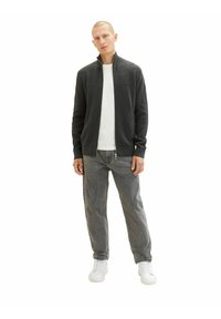 Szary kurtka zapinana na zamek z wysokim kołnierzem, noszona na białej koszulce z okrągłym dekoltem. Szare dżinsy i białe sneakersy dopełniają strój. Gładka faktura.