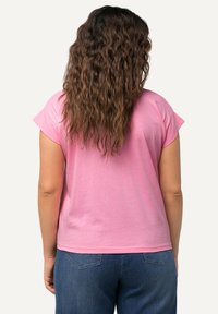 Světle růžové tričko s krátkým rukávem, volného střihu a s žebrovaným výstřihem, doplněné modrými džíny s jemným designem zadních kapes.