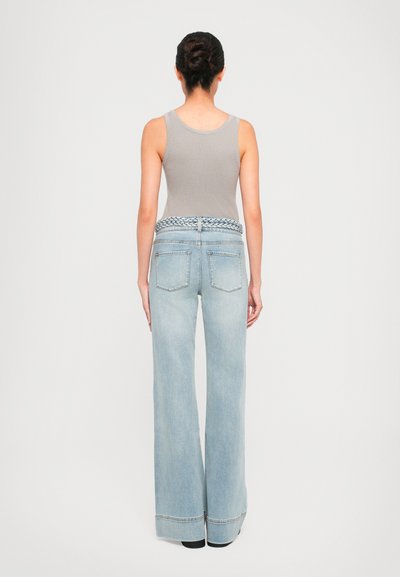Jean large bleu clair avec une ceinture tressée et deux poches arrière. Le haut est un débardeur gris ajusté en côtes.
