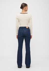 Light beige long-sleeve top with a black neckline, paired with dark denim flared jeans featuring a leather patch and two back pockets.