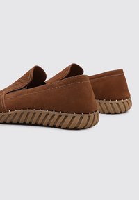Chaussures marron en cuir à enfiler avec une surface texturée, semelle en caoutchouc beige avec des stries, et couture contrastante le long des bords.