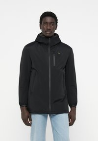 Schwarze leichte Jacke mit Kapuze, ausgestattet mit einem Frontreißverschluss, zwei Seitentaschen und einer Brusttasche mit gelben Akzenten. Glatte Textur.