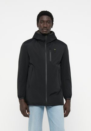 Zwarte lichtgewicht jas met capuchon, voorzien van een frontrits, twee zijzakken en een borstzak met gele accenten. Glad textuur.