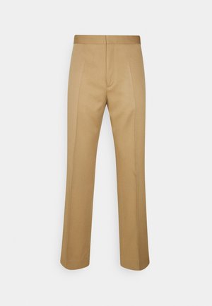 Beżowe spodnie na miarę z przednimi zakładkami, prostymi nogawkami i dopasowanym paskiem, prezentowane na jednolitym jasnym tle.
