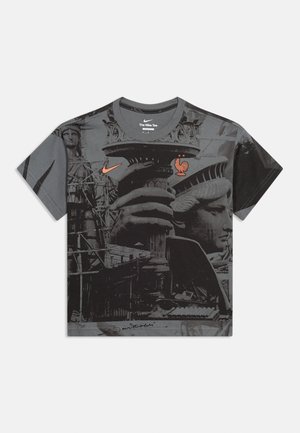 T-shirt avec impression en niveaux de gris de la Statue de la Liberté, logo Nike orange, et emblème orange de coq à deux étoiles sur la poitrine.