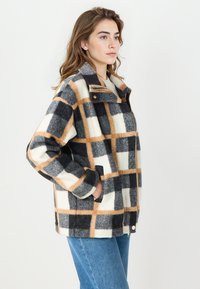 Geruite jas in grijs, wit en tan fleece. Beschikt over een hoge kraag, ritssluiting, twee zijzakken en een ontspannen pasvorm.