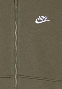 Sweatshirt com fecho em verde oliva feito de um tecido macio. Apresenta um fecho prateado e um logotipo da Nike em branco bordado na área do peito esquerdo.