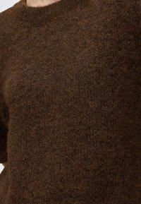 Gros plan d'une personne portant un pull en maille marron duveteuse avec un col rond.
