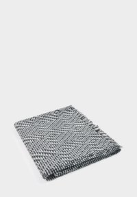 Coperta intrecciata in bianco e nero con motivo a zigzag, rifinita con bordi sfrangiati e una texture morbida.
