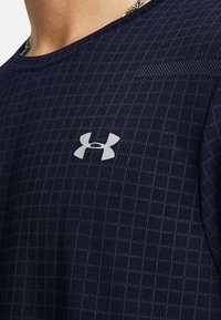 Mørkeblå kortærmet skjorte med et struktureret rutenetmønster, prydet med et lysegråt Under Armour-logo på brystet. Blød stofblanding.