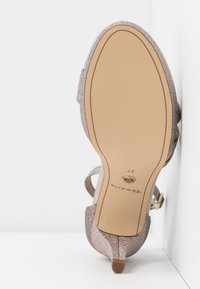 Shoe à talon haut en rose gold scintillant avec un bout pointu ; dispose d'une fine sangle à la cheville et d'un petit talon ; semelle beige lisse avec logo.