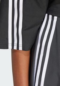Fekete sportpóló rövid ujjal, három függőleges fehér csíkkal az oldalszelem mentén és szövetanyag texture-el.