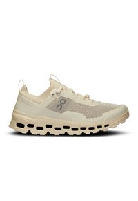 Chaussure de sport beige clair avec une tige en mesh, des accents texturés et une semelle épaisse et rembourrée présentant des découpes. Marquage minimal en gris.