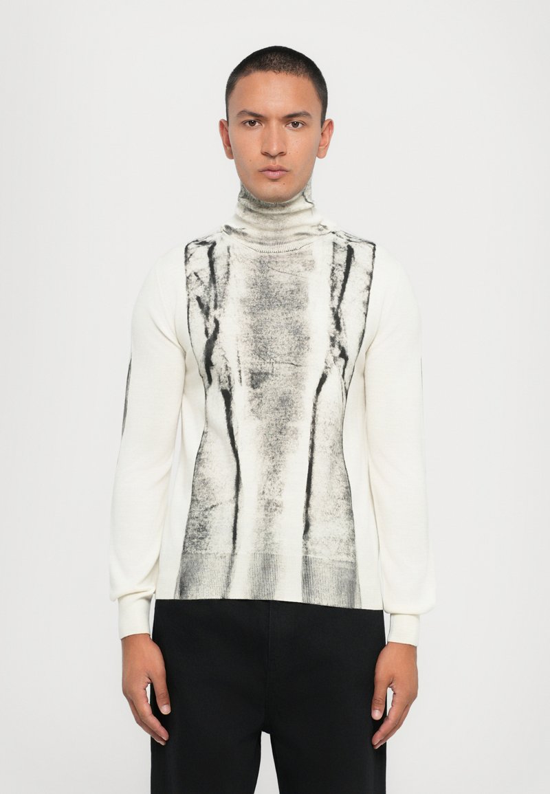 Κρέμα ρεγκλάν πουλόβερ με μαύρο αφηρημένο μοτίβο μπροστά, διαθέτοντας μακριά μανίκια και εφαρμοστή σχεδίαση.