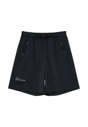 Młody mężczyzna w białej koszulce z krótkim rękawem z logo "Off Duty Gear", czarnych szortach, czarnych skarpetach i czarnych butach sportowych, stoi na białym tle.