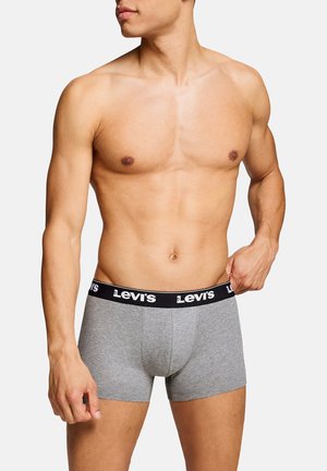 Oberkörperfreier Mann passt graue Levi's Boxershorts mit schwarzem Bund an, stehend vor schlichtem weißem Hintergrund.