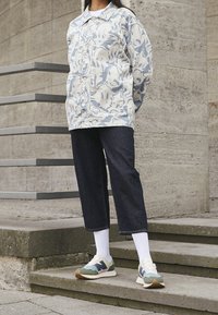 Lös passform, ljusblå mönstrad jacka över en vit skjorta, i kombination med mörka denimcroppade byxor och flerfärgade sneakers.