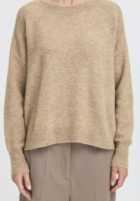 Beżowy sweter dzianinowy o luźnym kroju, z prążkowanymi mankietami i szerokim dekoltem. Miękka faktura z nieco dłuższym tyłem.