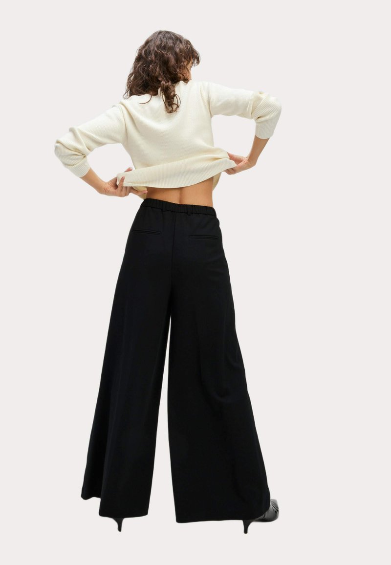 Abbigliamento femminile con un maglione a coste color crema e pantaloni larghi neri con vita elastica e tasche posteriori.