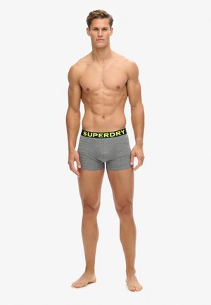 Boxer pantaloni grigi con una vita nera che presenta il testo giallo vivace "SUPERDRY". Il tessuto ha una texture morbida e un design a coste.