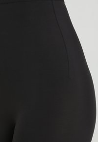 Black high-waisted leggings made of smooth, stretchy fabric with a subtle sheen. Features a flat waistband and seamless sides.